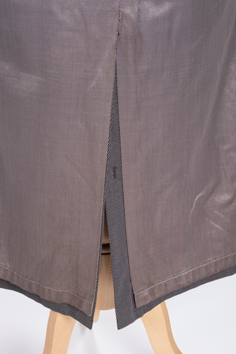 Rett frakk med slag og raglanerme. Foring av silke. Skjult knepping med fire knapper, kan også kneppe slaget under kragen. To lommer med klaff og to innerlommer. Splitt bak med knepping. Spensel nederst på ermene.