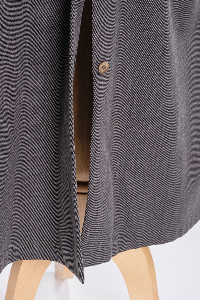 Rett frakk med slag og raglanerme. Foring av silke. Skjult knepping med fire knapper, kan også kneppe slaget under kragen. To lommer med klaff og to innerlommer. Splitt bak med knepping. Spensel nederst på ermene.