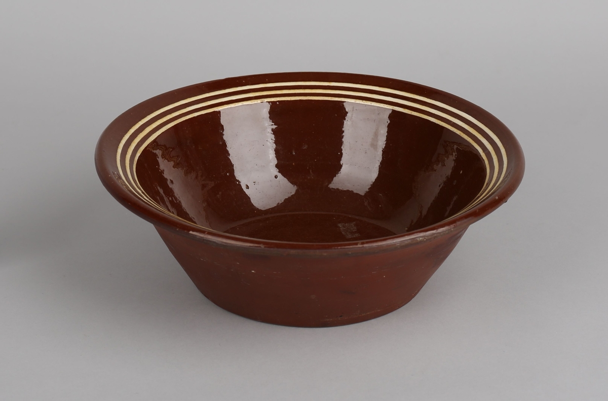 Rund bolle i brent leire, flat botn, skrånande sider flat munningsrand med dekor. Glasert inni.
