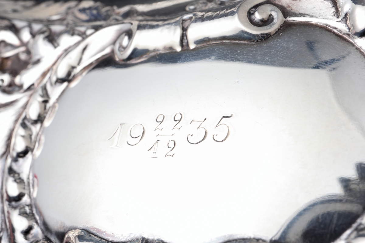 Fat av silver.
Ovalt prydnadsfat, med pressad dekor i hög relief på brättet, bestående av blommor och bladornament. Brättet är försett med två bekransade ramar, i den övre kanten är ett graverat monogram: "G B". I den undre kanten står: "19 22/12 35". På fatets baksida finns följande text: "Till Gunnar Borner på 50-årsdagen från kollegor i Kronobergs län". 
Stämplar på brättets undersida.

Inskrivet i huvudbok 1962