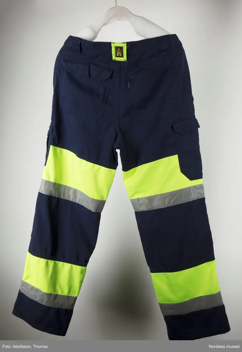 Mörkblå byxor som hör till arbetskläder för gruvarbete, tillverkade av  polyester (80%) och bomull (20%) med reflexband och varningsfärgat neongult tyg av polyester (65%) och bomull (35%). Till skyddsdräkten hör även en jacka. Plaggen är tillverkade av Grolls AB, märkta Björnkläder, EN 471. Med metallknappar, blixtlås och fickor (6 st).