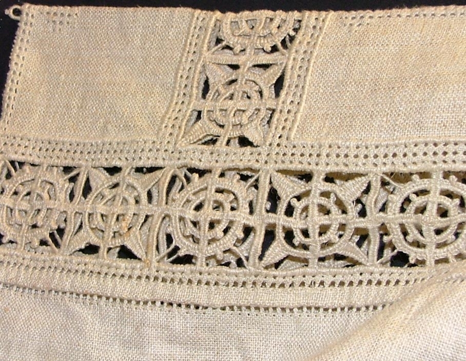 Av grov halvblekt linnelärft, två framstycken, ett bakstycke, besparing, korta ärmar skurna i ett med ovanstående stycken, bårder i spetssöm med grovt halvblekt lingarn kring besparing, hals och på ärmarna, samt hopdragssöm, s.k. myrgång, kring alla kanter samt på ryggstycket, i framkanten åtta sydda tränsar, knappar saknas, blusen rynkad mot smal midjelinning.

Tråckeltråd kvar i midjelinningen, knappar ej isydda.