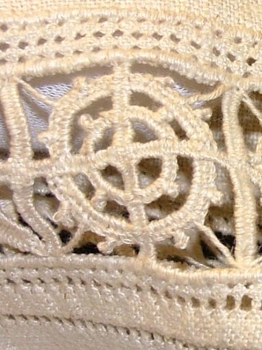 Av grov halvblekt linnelärft, två framstycken, ett bakstycke, besparing, korta ärmar skurna i ett med ovanstående stycken, bårder i spetssöm med grovt halvblekt lingarn kring besparing, hals och på ärmarna, samt hopdragssöm, s.k. myrgång, kring alla kanter samt på ryggstycket, i framkanten åtta sydda tränsar, knappar saknas, blusen rynkad mot smal midjelinning.

Tråckeltråd kvar i midjelinningen, knappar ej isydda.