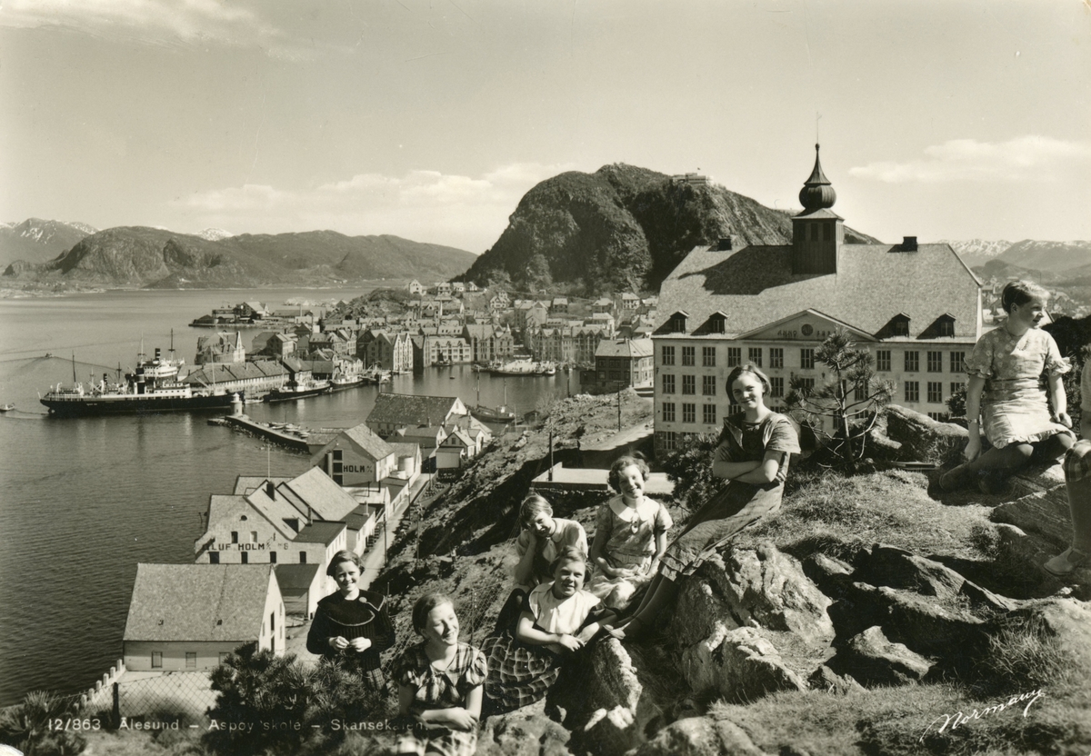 Prospektfotografi av Aspøy skole i Ålesund med byen og Skansekaia i bakgrunnen. I forgrunnen er ei gruppe barn som poserer for fotograf.