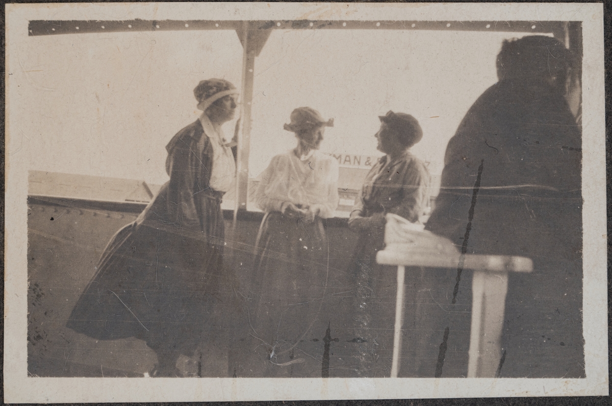 Tre kvinnor som står vid fartygets reling.
Bildtext: "Three wifes in a boat."