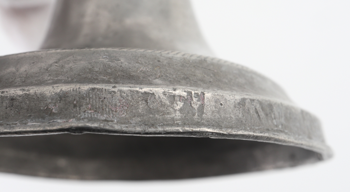 Ljusstake (2 st.) av tenn. 
Konisk ljuspipa med fast manschett. Låg klockfot, den ena med graverad bård. 
Stämplar (delvis otydliga) på fotens yttre nedre kant.

Inskrivet i huvudbok 1934.