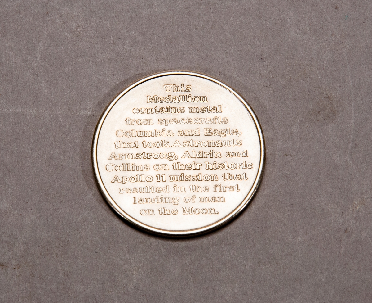 Åtsidan: Astronaut vid amerikanska flaggan vid den första månlandningen, text runtom: "The Eagle has landed July 20 1969". Baksida: "This medallion contains metal from spacecrafts Columbia and Eagle that took astronauts Armstrong Aldrin and Collins on their historic Apollo 11 mission that resulted in the first landing of man on the moon".