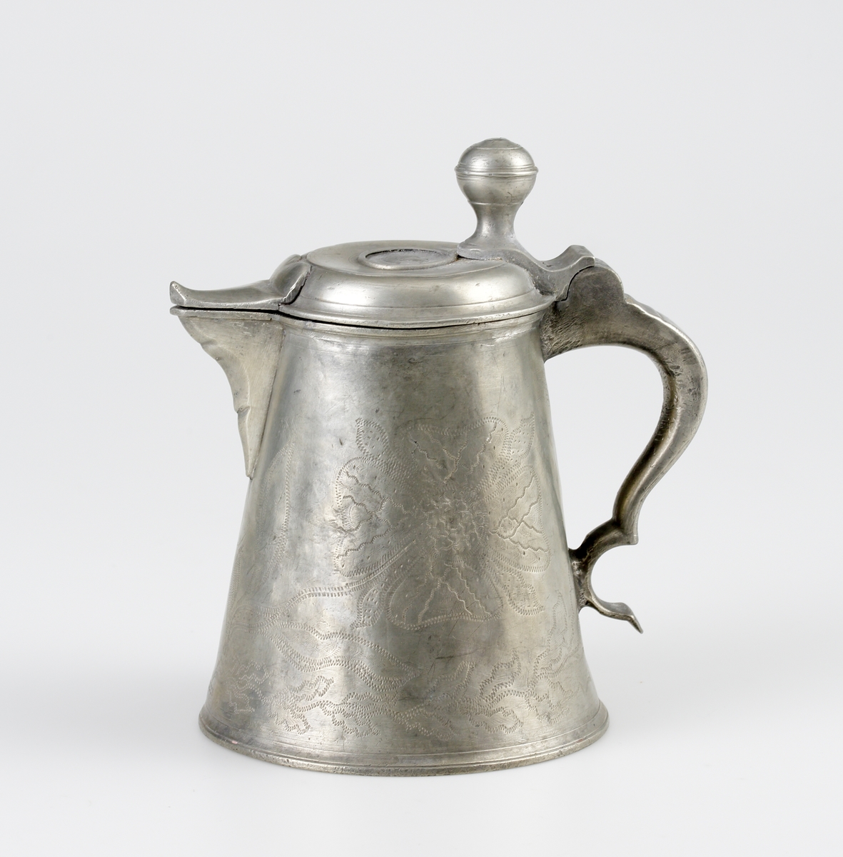 Stop av tenn.
Konisk modell. Svängd hänkel och tumgreppsknopp. Svängd, fasetterad snås. Fräcklad blomdekor på livet. På locket medaljong med Oscar I:s bild och inskriptionen: "Oscar, Sveriges och Norges konung". Stämplar på bottnens insida.

Inskrivet i huvudbok 1955.