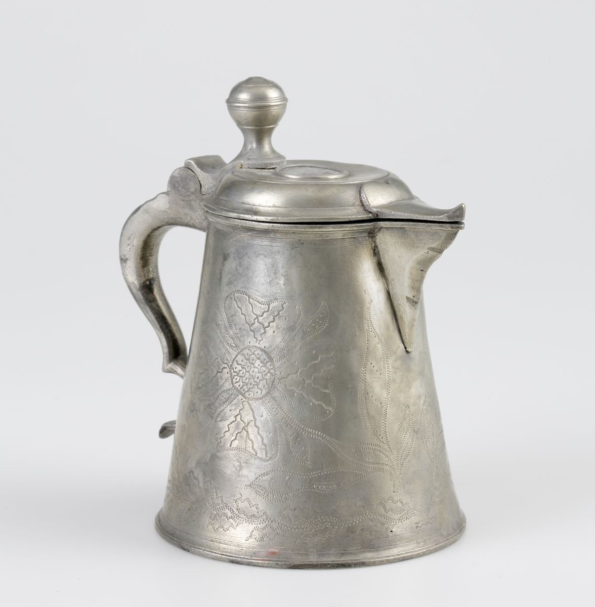 Stop av tenn.
Konisk modell. Svängd hänkel och tumgreppsknopp. Svängd, fasetterad snås. Fräcklad blomdekor på livet. På locket medaljong med Oscar I:s bild och inskriptionen: "Oscar, Sveriges och Norges konung". Stämplar på bottnens insida.

Inskrivet i huvudbok 1955.