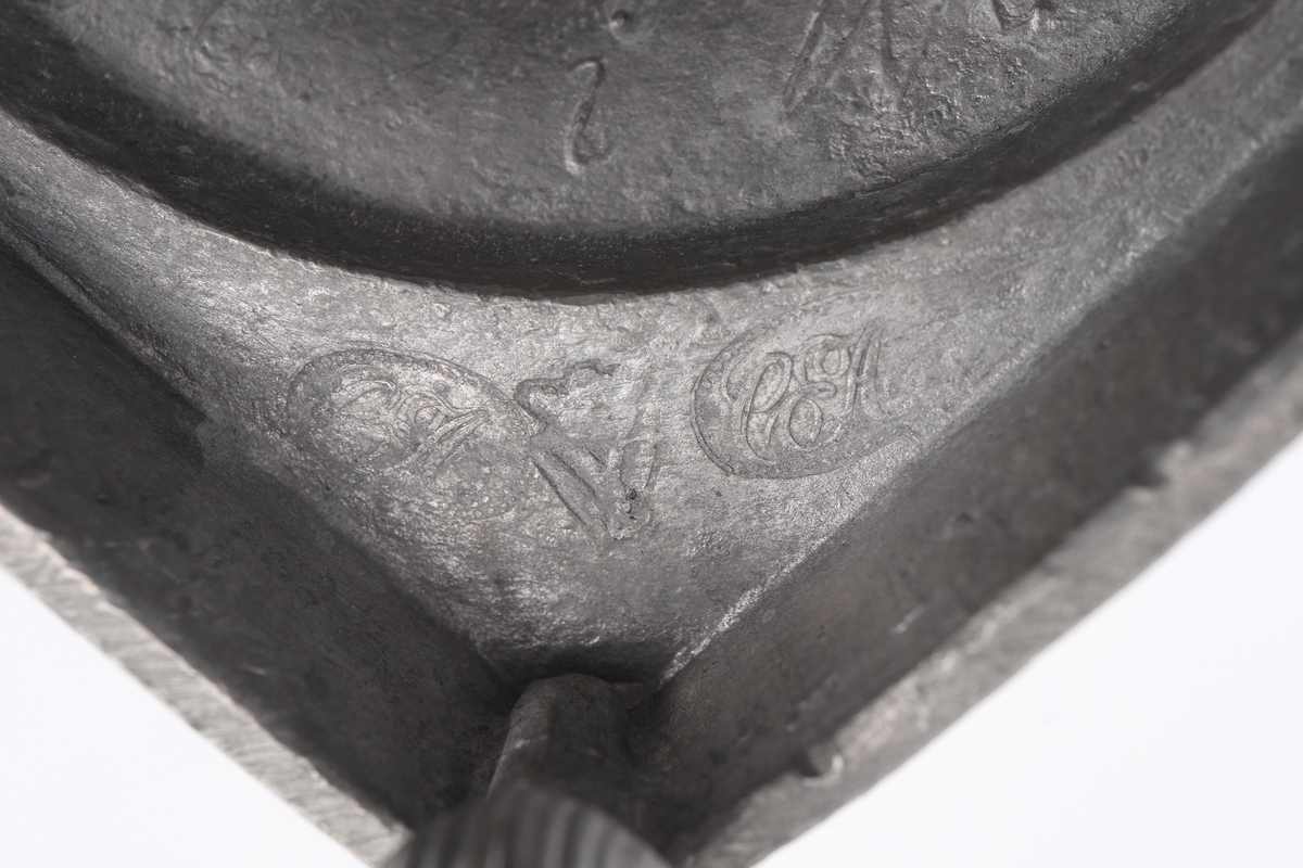 Ljusstake av tenn.
Empire. Räfflad urnpipa på klockat postament. Fyrkantig fotplatta med blombård, försedd med fyra kulfötter. 
Stämplar i botten + gjuten signering: "A i Wexiö".

Inskrivet i huvudbok 1937.