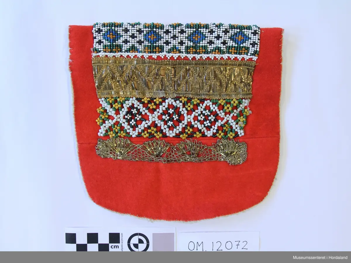 Bringeduk med mønster i border montert på raudt vadmål, annakvar perleborde og gullagraman 4 til saman, bakstykke av kvitt vadmål. Oppe er bringeduken bretta ned der som det har vore ein grøn kant; det viser restar av det grøne stoffet. Den øverste perlekanten er akkurat i bretten.