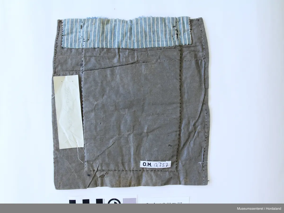 Brodert med ullgarn i plattsaum. Alt er handlaga. Hovudmotiv er små åttebladroser i border. Oppe er det påsydd eit blått silkeband med eit breitt gullband (i forgylt sølvtråd) utanpå silkebandet. Alt er montert på eit tynt, vokset bomullslerret. Oppe på baksida er det eit ekstra bomullstoff (blåstripet). Bokstavane BODM er broderte inn nede på bringeduken i kross-sting.