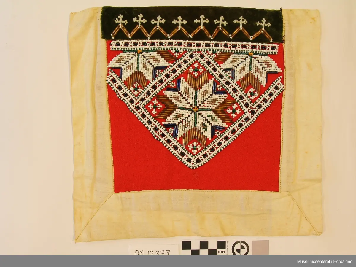 Kvadratisk bringeduk med ei heil og to halve åttebladroser i perler på raudt ullstoff. Mørkegrønt fløyelskant oppe med sikk-sakk bord stråperler. Bomullstoff til bakstykke. Montert med maskinsaum. Innlagt tynn papp som forsterking.