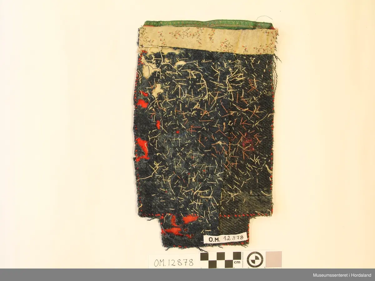 Rektangulær brineduk med perlebroderi/perlenett på raudt ullstoff. Skjøtt på eit lite stykke nede i eit tynnare ullstoff.  Silkeband oppe til kant. Bakstykke av blå ullkypert, fillete. Bomullstoff i øvre kanten bak bandet til forsterking.