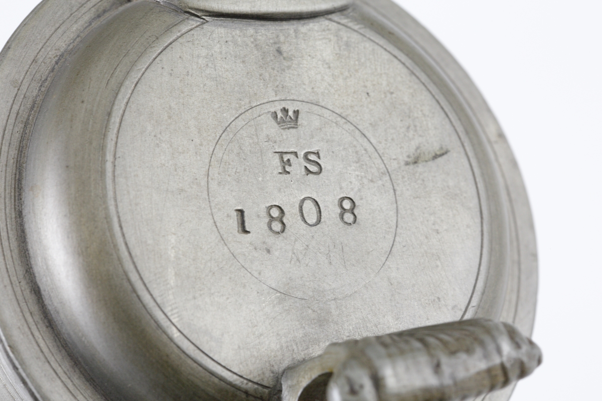 Stop av tenn.
Konisk, bandad modell. Svängd hänkel och ornerat, svängt tumgrepp. Svängd snås. 
Ovanpå locket är stämplat en krona, ägarinitialer: "FS" och årtalet 1808. 

Inskrivet i huvudbok 1982.