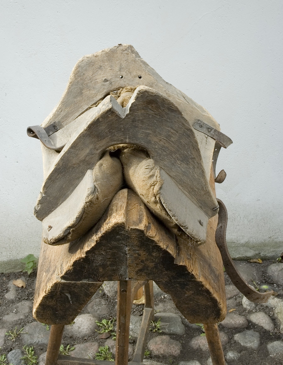 Klövjsadel med sido- och tvärstycken av trä. Mittdelen består av säckväv, stoppad med krollsplint. Båda tvärstyckena (eller valven) har en toppig form, det bakre är avhugget och det främre har ett v-format urtag. Nertill på tvärstyckena finns avlånga hål, troligen för remmar. Fyra korta spännremmar finns fortfarande kvar på sadeln. I bakre tvärstycket finns två hål där det troligen suttit en bygel.