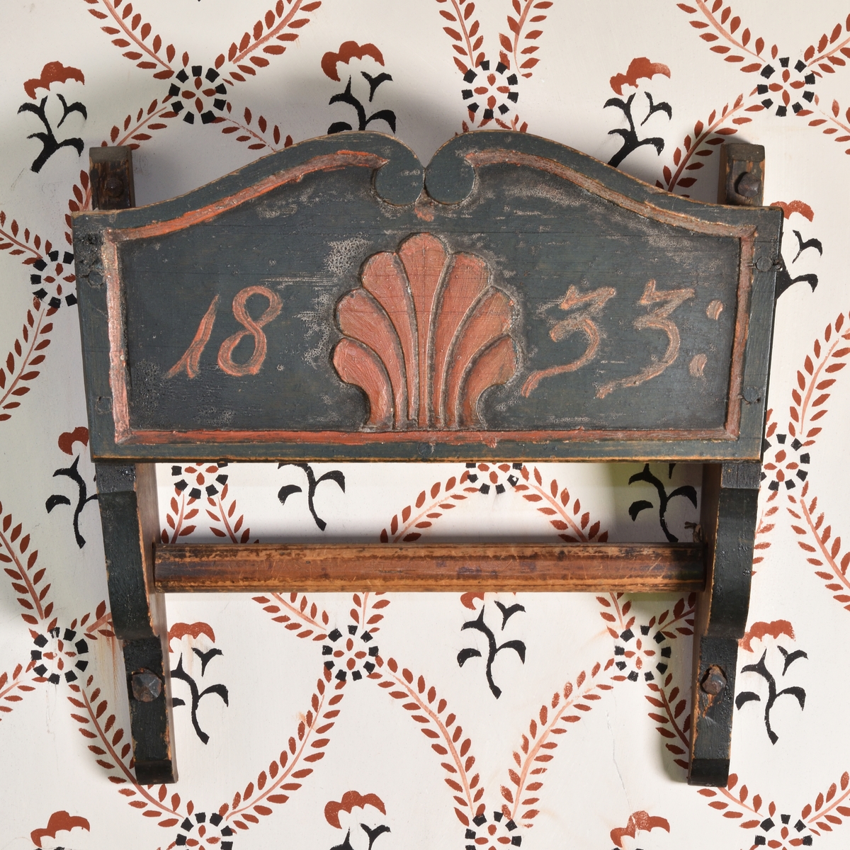 Handklähylla av furu, målad mörkgrön. Formad som en öppen låda med sidor och botten. Förlängda sidogavlar, nedtill profilerade, med instucken hängstång. Framsidan med snidad rocaillesnäcka i rött samt årtalet "1833".