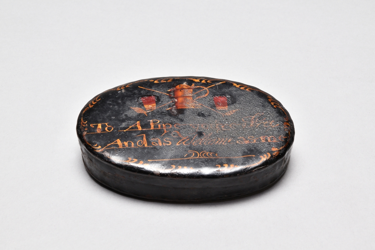 Tobaksdosa av järnplåt, oval, med tättsittande lock. Svartlackerad. Dekor i gulrött i form av 2 korslagda långpipor, ett stop och 2 dricksglas samt bård i gyllengult.