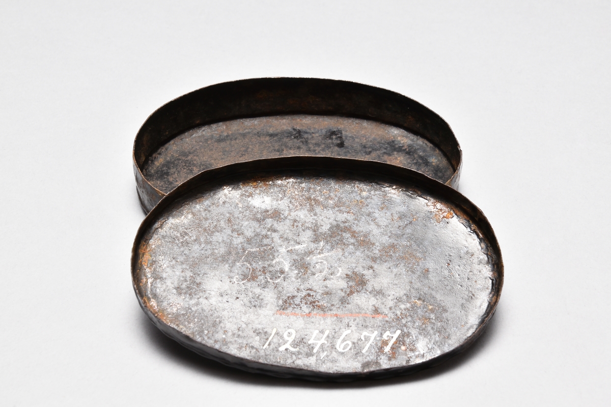 Tobaksdosa av järnplåt, oval, med tättsittande lock. Svartlackerad. Dekor i gulrött i form av 2 korslagda långpipor, ett stop och 2 dricksglas samt bård i gyllengult.