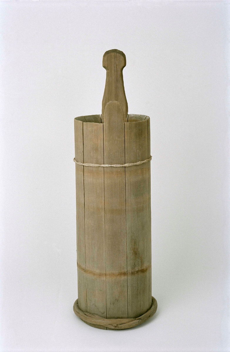 Ljuskärna, laggad av gran, omålad, cylindrisk. Två stavar förlängda, varav en utgör ett handtag, enkelt profilerat. Nio stavar, fyra vidjor, varav tre saknas. Lock saknas. Under botten ett svagt inristat B. Kan även ha använts som smörkärna.