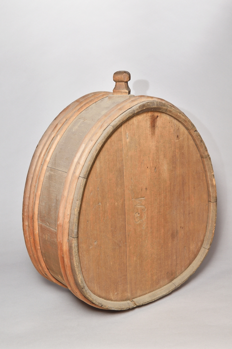 Mjölkflaska, laggad, av barrträ, omålad, oval med platta sidor. I toppen ett fyrkantigt sprund, lös tapp med täljd knopp. Fem laggband av ene, varav ett saknas. Inristat "IE 1816" , "PMI" (?) samt ett bomärke.