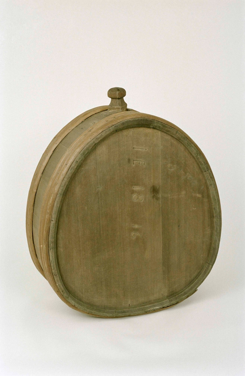 Mjölkflaska, laggad, av barrträ, omålad, oval med platta sidor. I toppen ett fyrkantigt sprund, lös tapp med täljd knopp. Fem laggband av ene, varav ett saknas. Inristat "IE 1816" , "PMI" (?) samt ett bomärke.