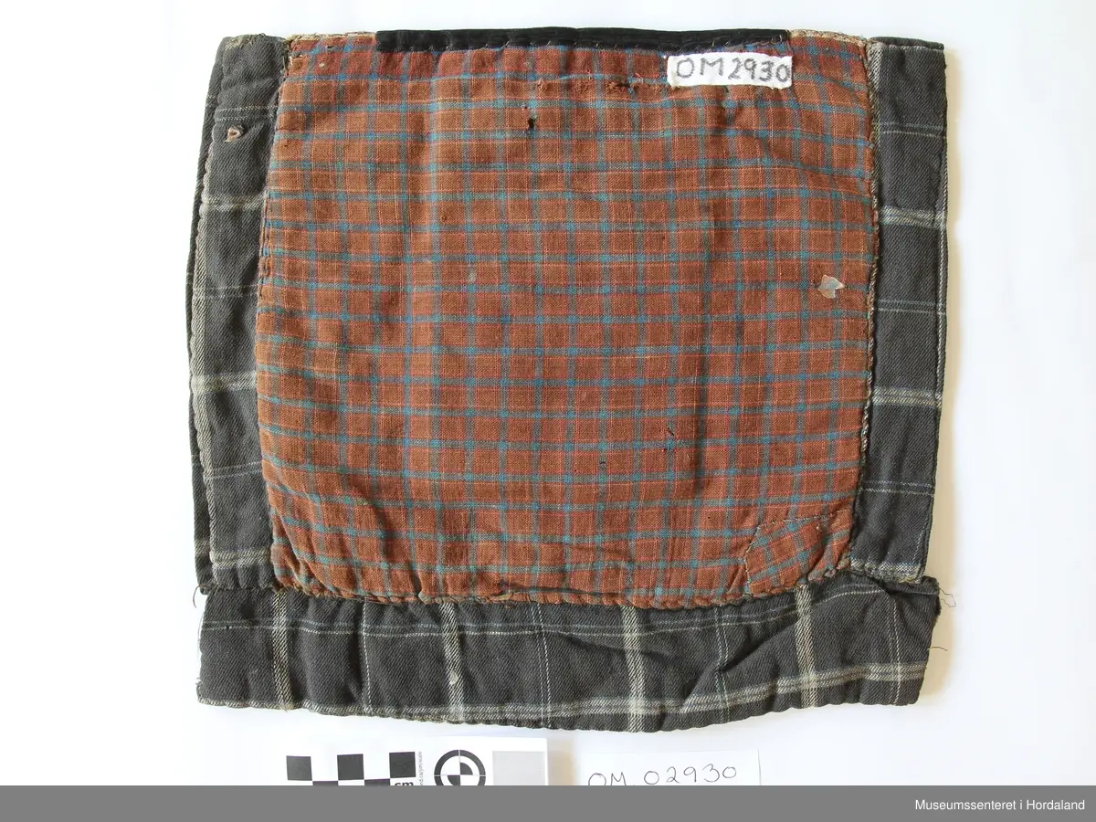 Rektangulær brystduk på kvadratisk botnstykke. Brystduken er brodert med halve kross-sting på stramei. Blomstermotiv i mange skarpe fargar. Ein svart silkeband oppe. Bomullstoff til botnstoff, bakstykke og sidestykke og stykke nederst. To forskjellige stoff til botn stoff med ruter. Brystduken er forsterka inni med tjukk kypertstoff.