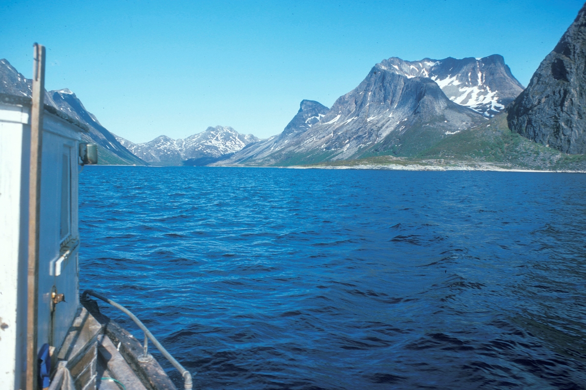 Flakstadvåg, 1976 : I forgrunnen, deler av styrhuset på en båt. I bakgrunnen ser vi Indre Selfjord, ved foten av høye fjell.