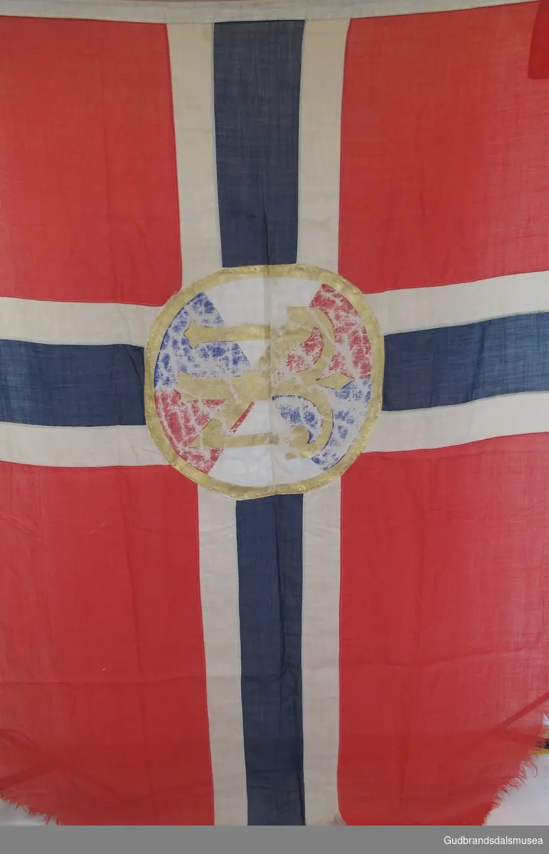 Norsk flagg med Den norske turistforenings logo påmalt i midten. Innsydd line øverst med metallhengsel i ene enden. I bruk på¨Sandhaug turisthytte frem til 1948.
