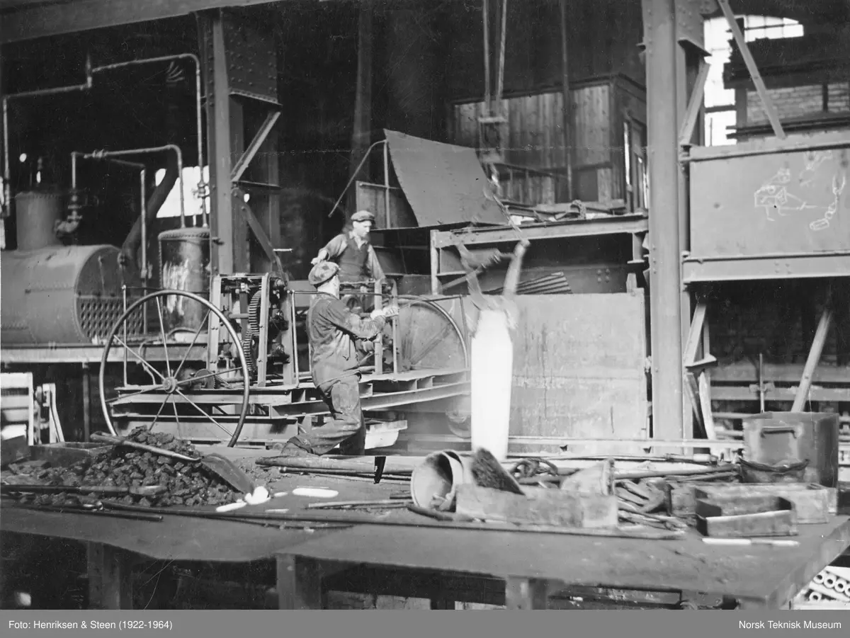 To arbeidere ved Christiania Spigerverk løfter en blokk fra varmegropa for å føres til utvalsing.