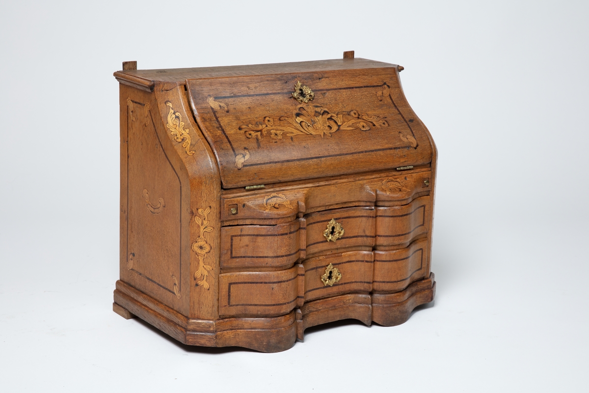 Barneskatoll i rokokkostil med separat overskap og underskap samt felles nøkkel til begge deler. Underskap med kraftig buet og profilert front, to skuffer samt nedfellbart pultlokk med hylle-, skap- og skuffseksjon innenfor. Overskap med to rette dører og kraftig profilert, delvis gjennombrutt gesims. Både over- og underskapet rikt dekorert med intarsia av høy kvalitet med rocailler, skjell, konturlinjer og blomsterornamentikk. Dekorative skilt av messing rundt alle nøkkelhull. Initialer og årstall på skapdør bak pultlokk. Skatollet står på to lave føtter.

A: underskap
B: nøkkel
C: overskap