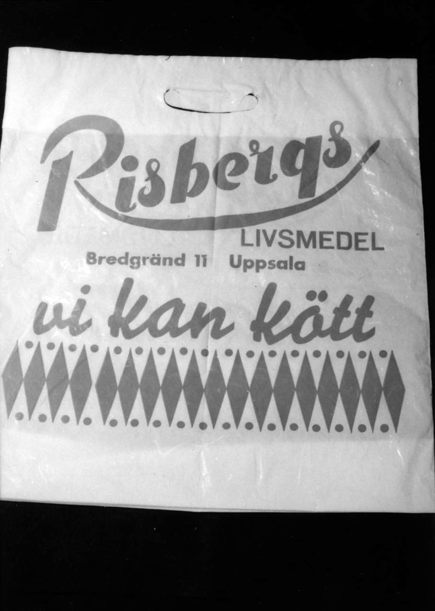 Bärkasse av plast, plastkasse, vit med röd text: Risbergs LIVSMEDEL, Bredgränd 11, Uppsala. Vi kan kött, på båda sidor.