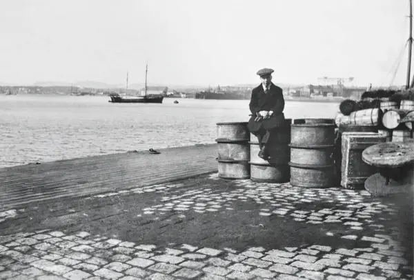 Ung gutt sitter på en oljetønne på kaien i Kristiania. Foto: MiA.