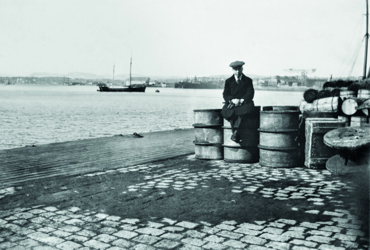 Ung gutt sitter på en oljetønne på kaien i Kristiania. Foto: MiA.
