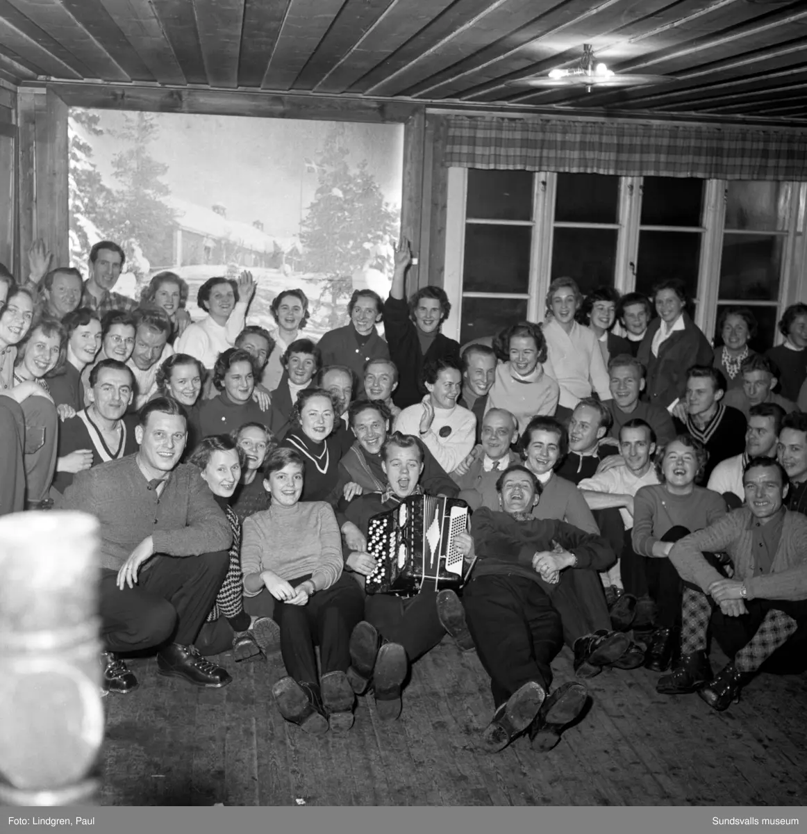 Skidklubben Vidar på utflykt till Hulistugan. Underhållning med servering och pjäxdans. På bild 1 ses en tavla föreställande Klissbergsstugan på väggen bakom gruppen. På bild 5 ses några personer visa upp en affisch med skidmärket Snöstjärnan som introducerades av Svenska Skidförbundet detta år.