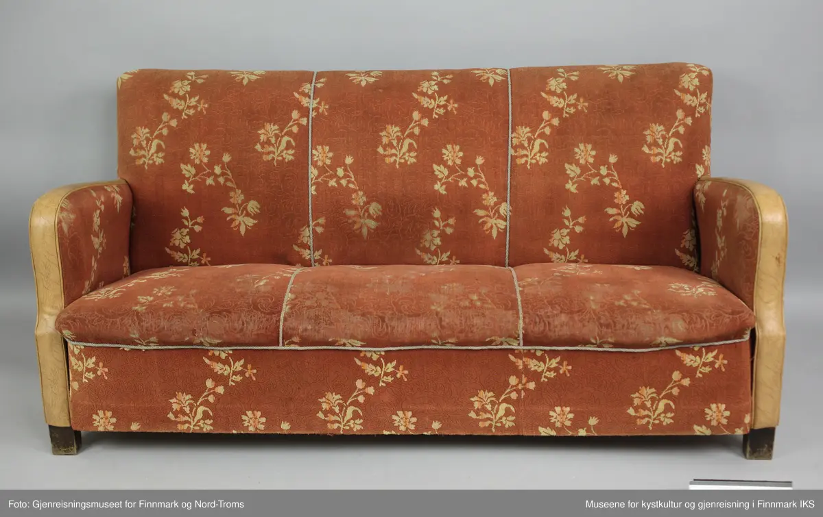 Sofaen er en treseter der rygg og setet er avgrenset med tvinnede pyntebånd i grått. Rygg, sete og armlener er polstret og trekt med et stoff som har rødbrun bunnfarge og et lysebrunt blomstermønster. Trekket er spikret til ramma på undersiden og på armlenen på utsiden. På kanten er armlenene trekt med lysebrun kunstskinn. På undersiden er sofaen lukket med plater, slik at polstringa ikke er tilgjengelig. Det er likevel synlig at sofaen består av en ramme med to tverrforbindelser. Dette er et inngrep som mest sannsynlig er gjort for å få støttet opp under sylinderfjærene. 