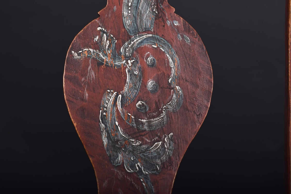 Stol av björk och furu, på fyra svängda ben. Ryggen har en mittbricka i balusterform. Stolen är målad i mörkt rött och ryggbrickan har målad dekoration i rokokostil i grått och vitt.