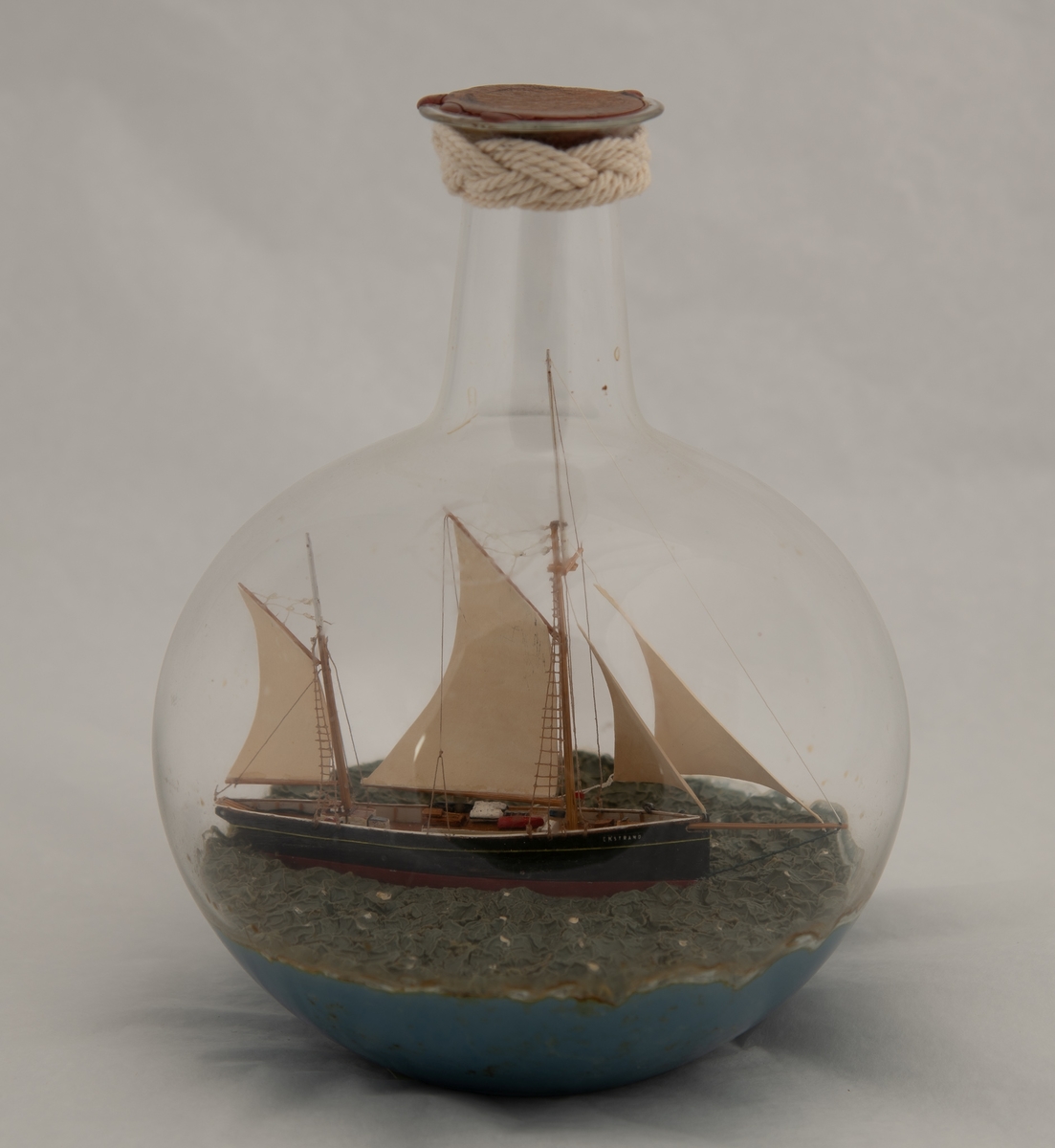 Flaskeskute: "Ekstrand" , galeasrigget kutter , før ombyggingen i 1990.  Kuleformet flaske av klart glass . Sortmalt skrog , rød under vannlinjen , hvit kant , hvite seil. Lys blågrønn kruset sjø.