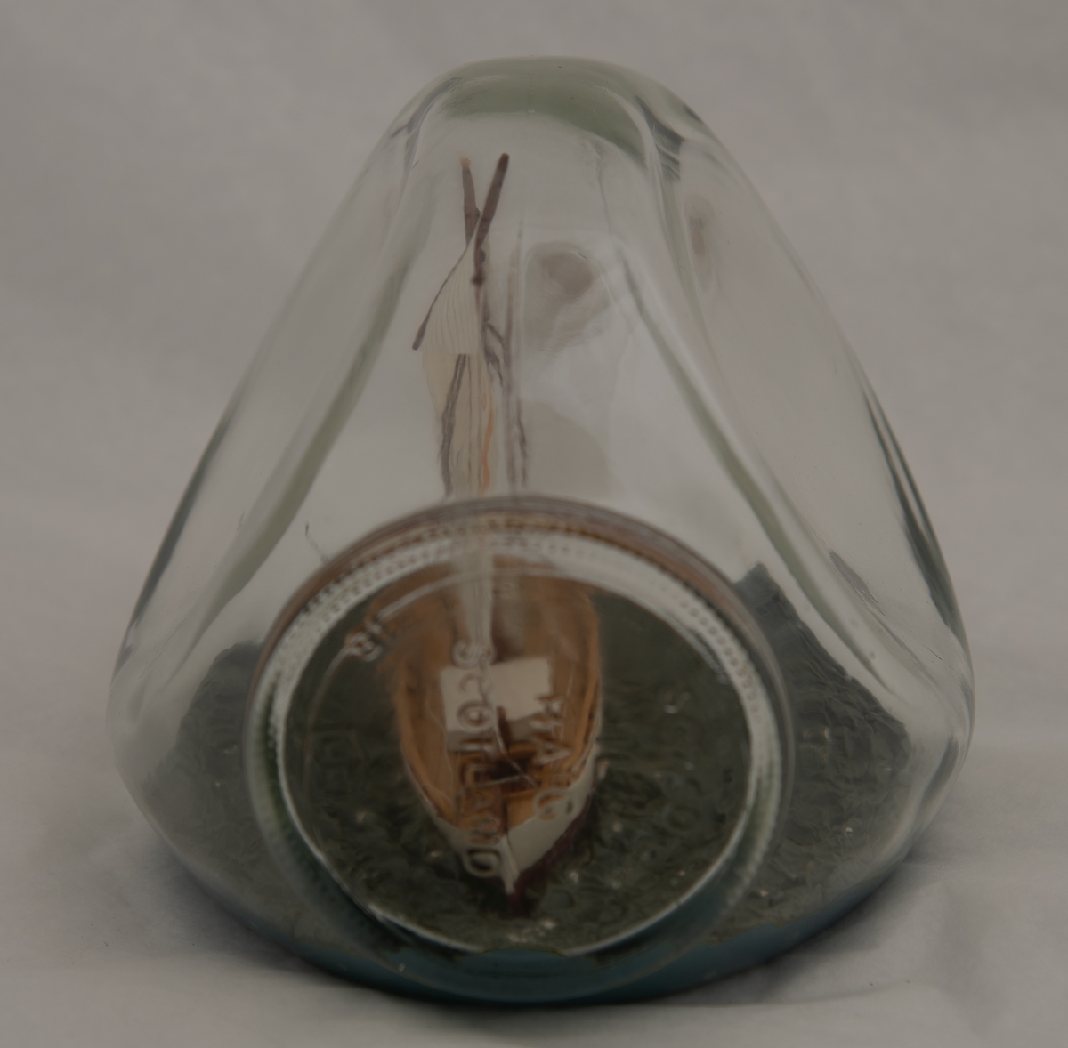 Flaskeskute: "Krabben" , losbåt nr. l (Colin Archer)  Flaske i klart glass med trekantet form.  Hvitmalt skrog , brun under vannlinjen. Seil med oransje stripe og tallet 61 i oransje. Blågrønn sjø.