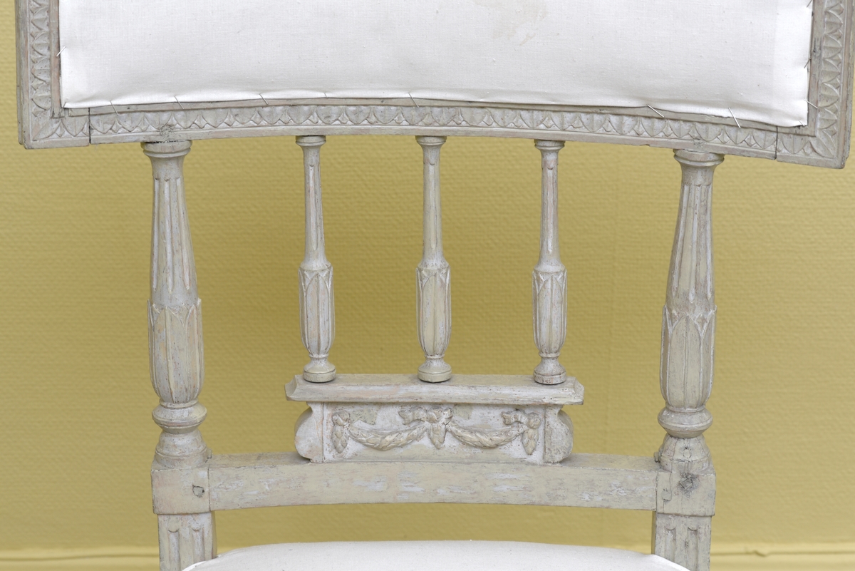 Gråvit stol i gustaviansk stil av björk på runda, avsmalnande ben. Benens övre del är dekorerade med bladkrans. Den främre sargen är något svängd och dekorerad med en äggstavslist. Den rektangulära ryggbrickan bärs upp av totalt fem, tre mindre och två större, ståndare. Ryggbrickans ramvirke är dekorerad med äggstavslist. Stolen är provisoriskt klädd på sits och i rygg med ett vitt bomullstyg.