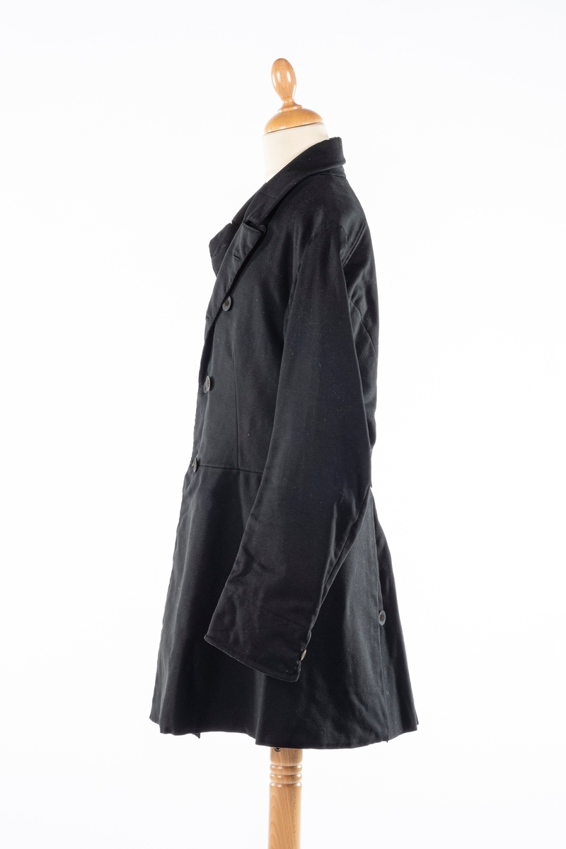 Dobbelt spent frakk som kneppes med fire knapper på hver side. De øverste kan ikke kneppes. Knappene er kledd med silke med fløyelsornament i midten. Hempe i nakkelinning. Det er splitt med legg fra livet og ned, med en knapp over splitten på hver side. Det er også to knapper lenger ned i splitten, og en knapp på hver mansjett. Frakken er foret.