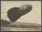 Bilden visar en ballong med järnkors symbolen som dras ner till marken av en grupp soldater. Till höger ser man vagnar med teknisk utrustning.