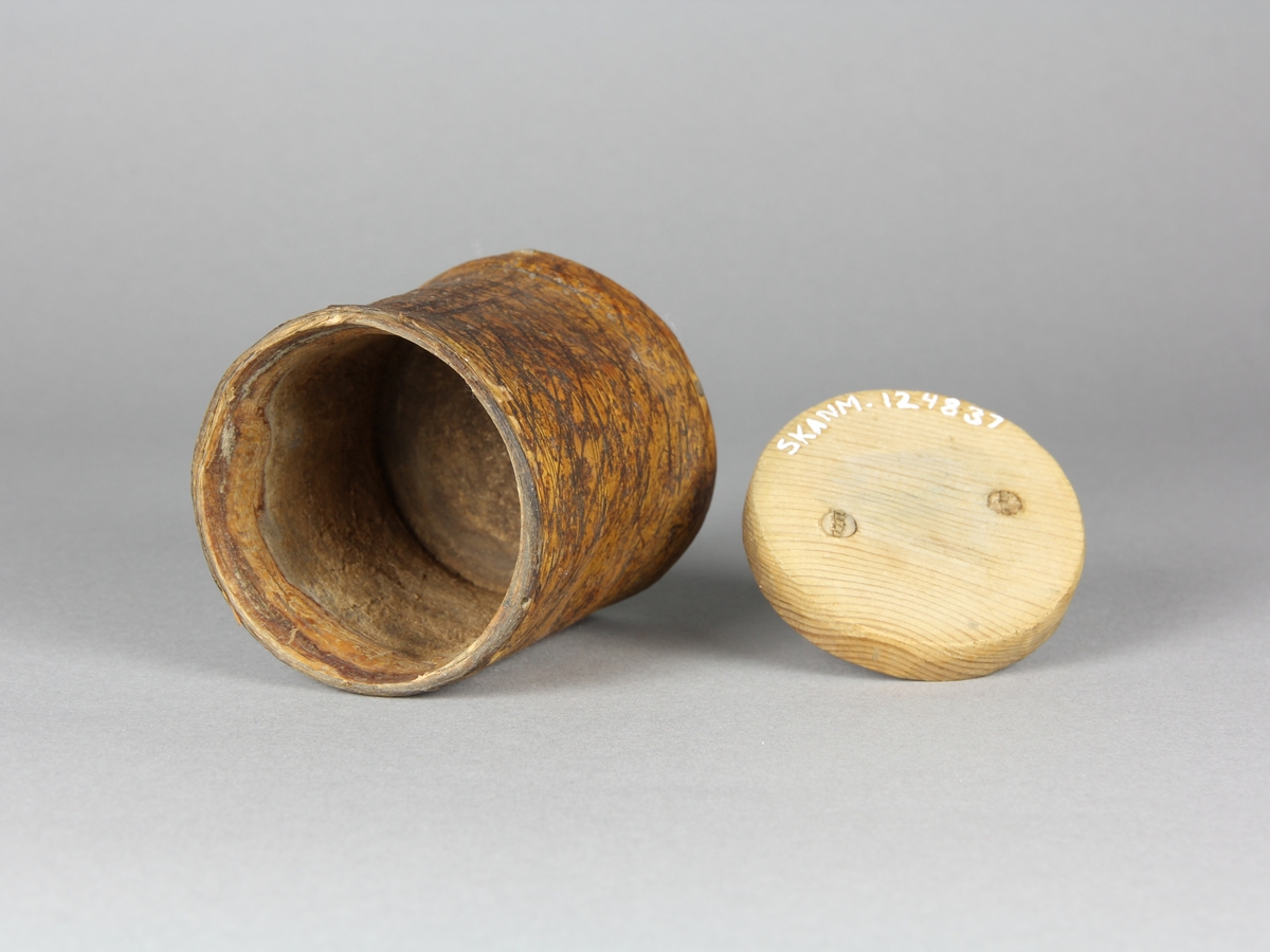 Snusburk, cylinderformad av hel näver med lock och botten av furu. Nävern ornerad i rut- och prickmönster. Näverändarna fästa genom att de tampats och flätats ihop. På locket tvärgrepe av enträ som kilats fast från undersidan. Snusrester i botten.
