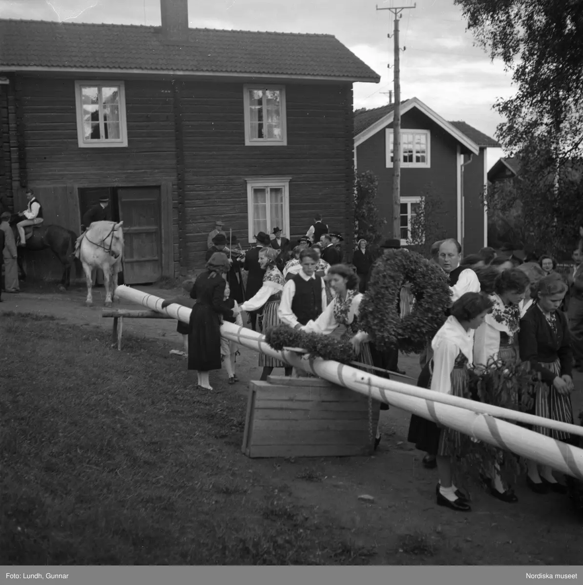 Motiv: (ingen anteckning) ;
En kvinna och två män spelar boccia, porträtt av en kvinna i folkdräkt, en folksamling står vid en gärsgård, tre män i folkdräkt rider på hästar framför män som spelar fiol och kvinnor i folkdräkt som går på en väg "Midsommartåget till Tibble", en kvinna i folkdräkt rider på en häst som drar en vagn med barn, kvinnor och män pryder en midsommarstång med lövade ringar.dju