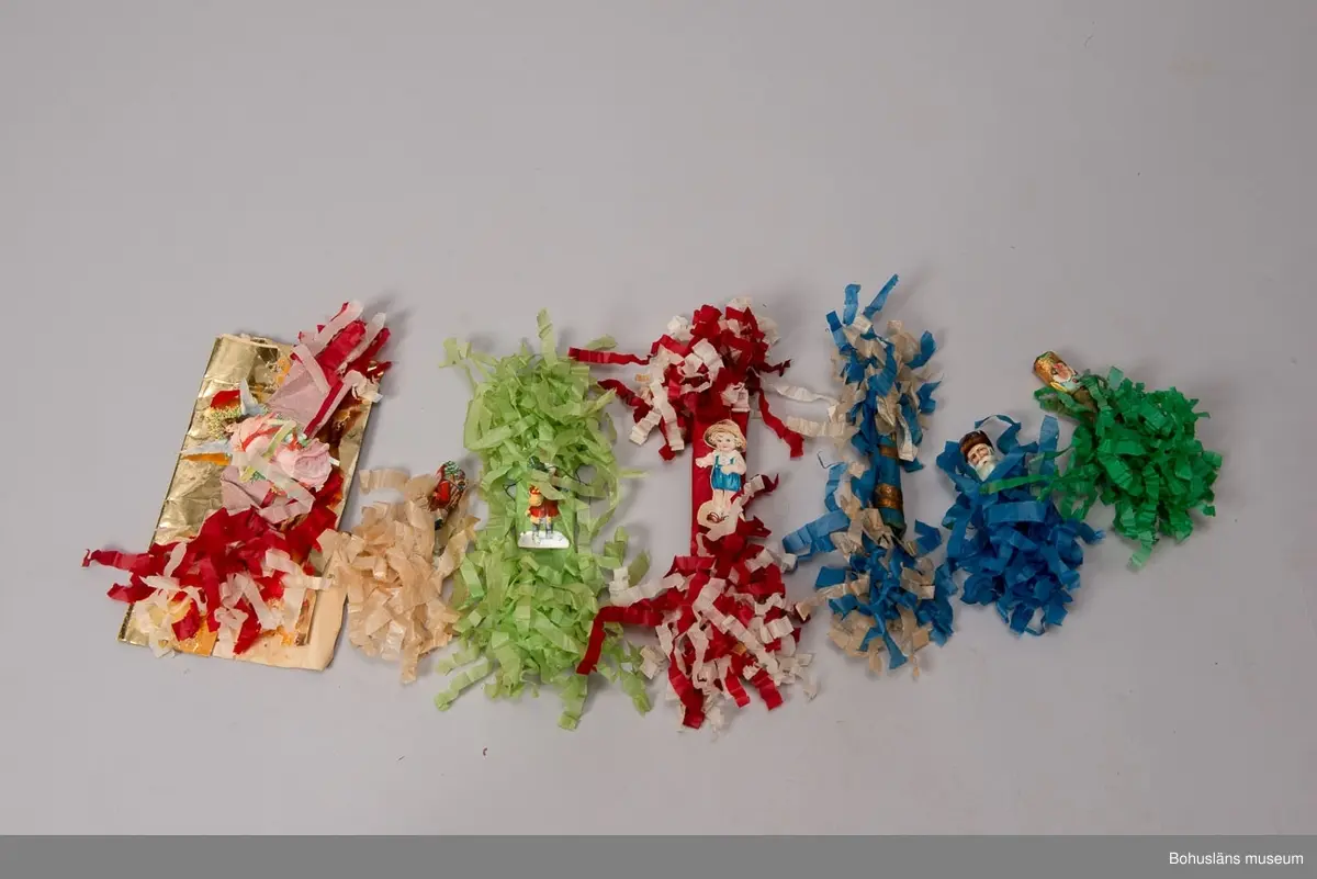 Låda av brun papp. På locket påklistrad,delvis bortsliten etikett med text: "Herman Radyn Uddevalla". Lådan innehåller: 19 st. julgransljushållare, glitter i silver, glitterband i guld, 7 st. julgranskarameller av papper, 1 toppstjärna, 12 st. hjärtan av papper i olika färger, 6 st. små glasbollar i sytråd, svenska flaggor i tråd, 12 st. svenska flaggor med järntråd,