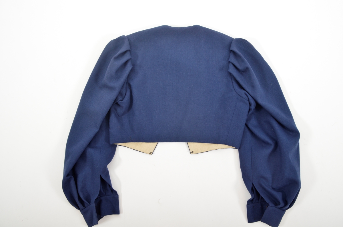 Grafferbunad med raudt damaskvove ulltøy i livet, og blått toskaftvove ulltøy i stakken. A. Livet har opning framme festa saman med tre hekter og krokar. Saum midt bak, og med to svinga ryggsaumar. Fóra med ubleikt halvlin.
Stakk i toskaft-vove ulltøy, brodert med ullgarn i forskjellige fargar. Rosemotiv. Den er foldelagt. Brei skonnering av svart bomulltøy i  nedrekanten.
B. Jakke i blått toskaftvove ulltøy. Opning midt framme med tre hekter og krokar til lukking. Eit snitt på kvar side. Erme er foldelagt oppå skuldera og nede ved ermekragen. 
C. Lue, pullue, i same tøy og broderi som stakken. Fóra med ubleikt halvlin. I nedrekant av pullen løpegang med rynka strikk. 
D. Lomme i same tøy og broderi som stakken. Sølvforgylt lommelås.