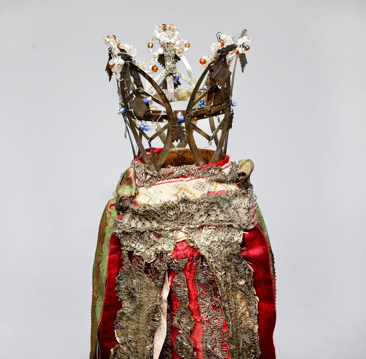 Brudekrone i metall med fem spir. Krona er pyntet med metallheng og glassperler. Det er påsydd valk nederst, med brodert bånd og metallknipling rundt valken.

Bak på det broderte båndet rundt valken, er det festet bånd. På midten er det et bredt bånd i rødt med metallkniplinger, med brede bånd med lys bunn og med en rød kant vendt ut fra den røde midtbåndet. Metallkniplinger er festet til de tre brede båndene. Deretter fire smalere bånd på hver side av de brede båndene. Disse er festet samlet med en liten sløyfe på det bredeste der det er festet på valken. 

En plastkam er påsydd valken sammen med to hvite, nyere bånd. Antagelig gjort i nyere tid for å feste krona og knyte under haka.