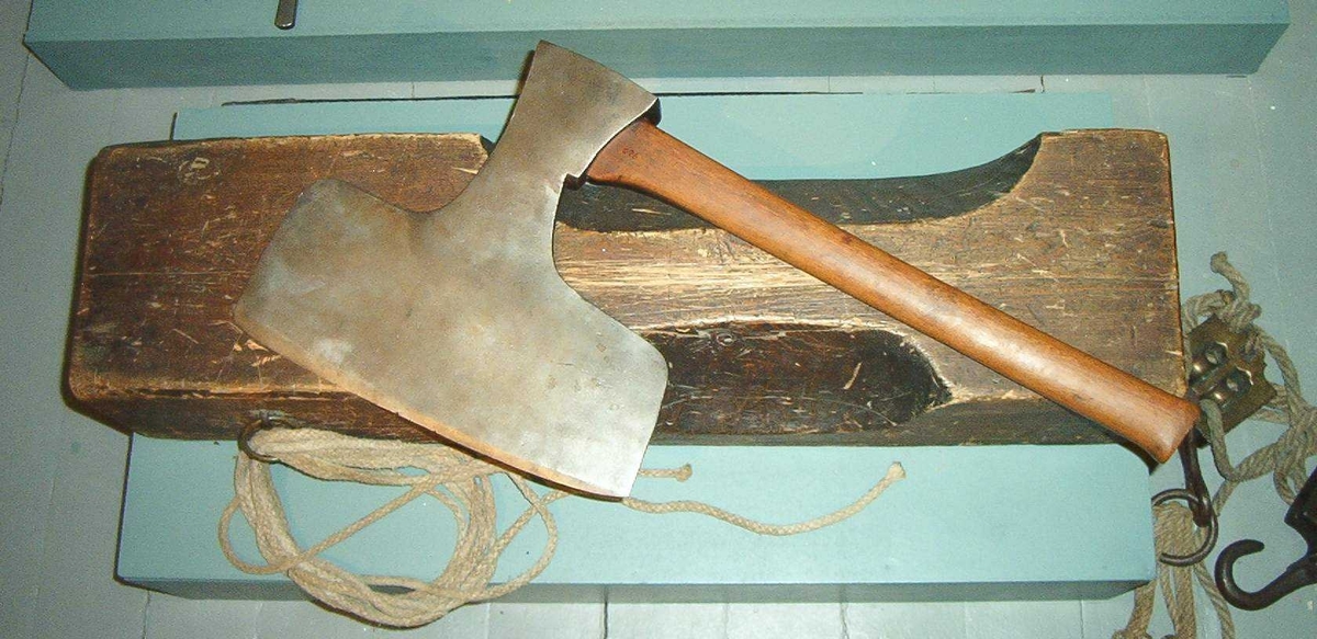 Skåret rektangulær treblokk med et smalt søkk til haken og et bredere søkk for halsen. Huggemerker og slitasje mellom de to søkkene.