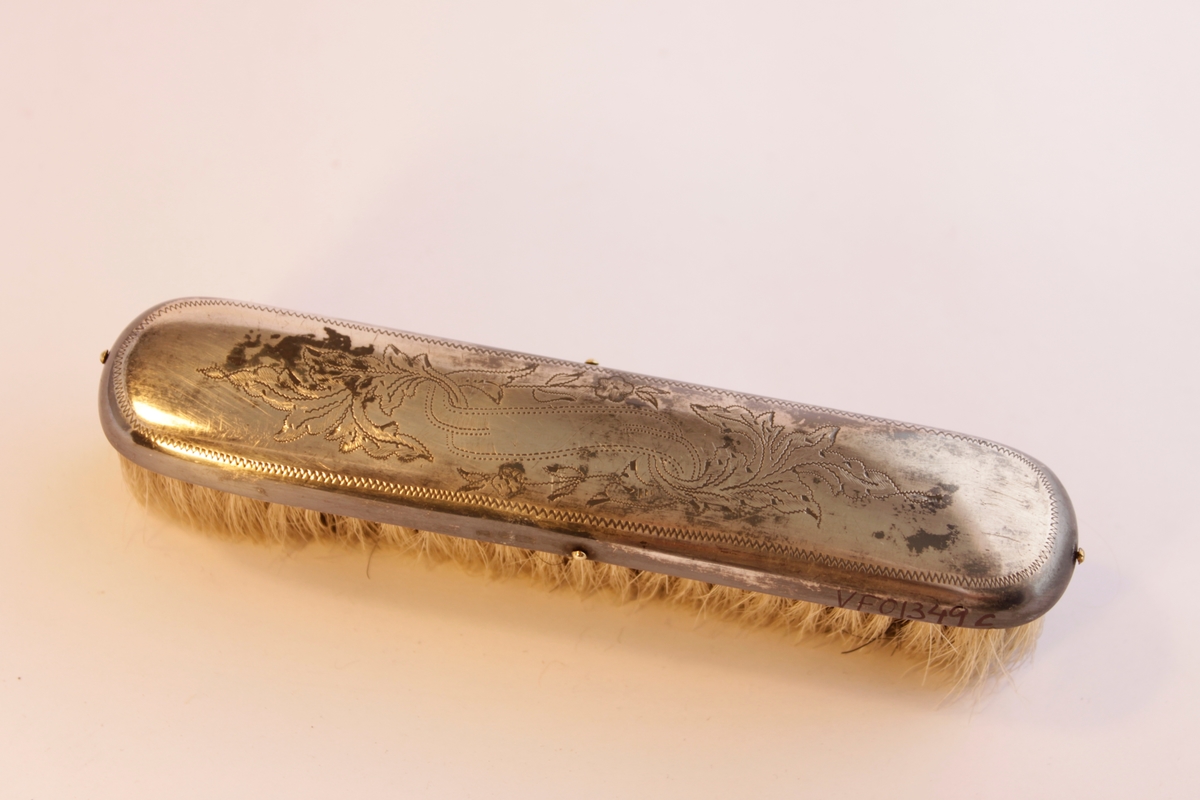 Borstgarnityr bestående av tre borstar en (a) hårborste, två klädesborstar (b-c). Naturborst. Borstarna är klädda i nysilver som har ingraverade stiliserade blommönster. Hårborsten och den ena klädborsten har namnet "Axel" ingraverat på ovansidan. Själva borsthuvudena är tillverkade av trä och sedan har en plåt av nysilver spikats på.