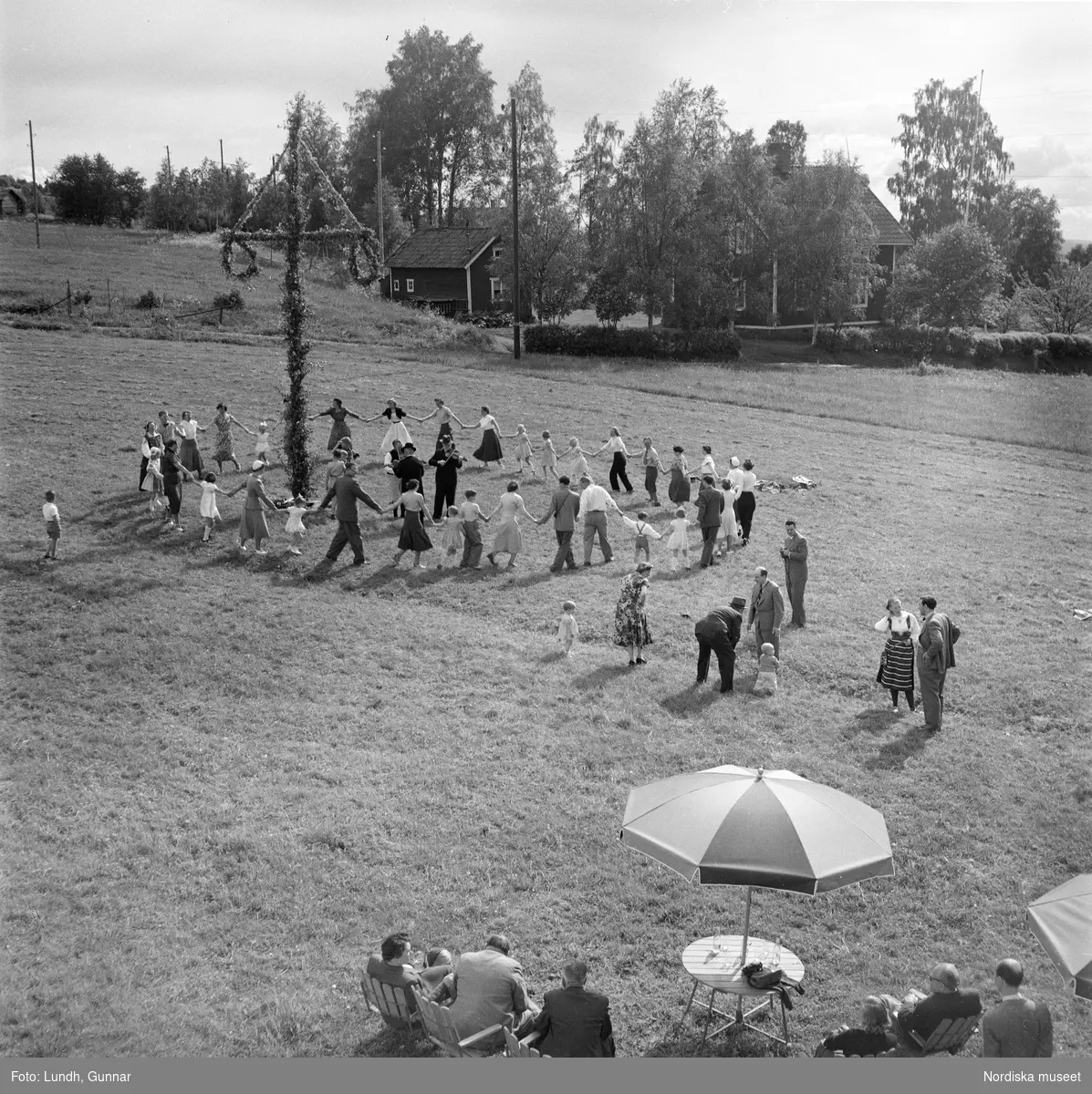 Motiv: Lerdalshöjden ;
Porträtt av en flicka som håller blommor, vuxna och barn dansar runt en midsommarstång, tre män i folkdräkt spelar fiol vid en midsommarstång.